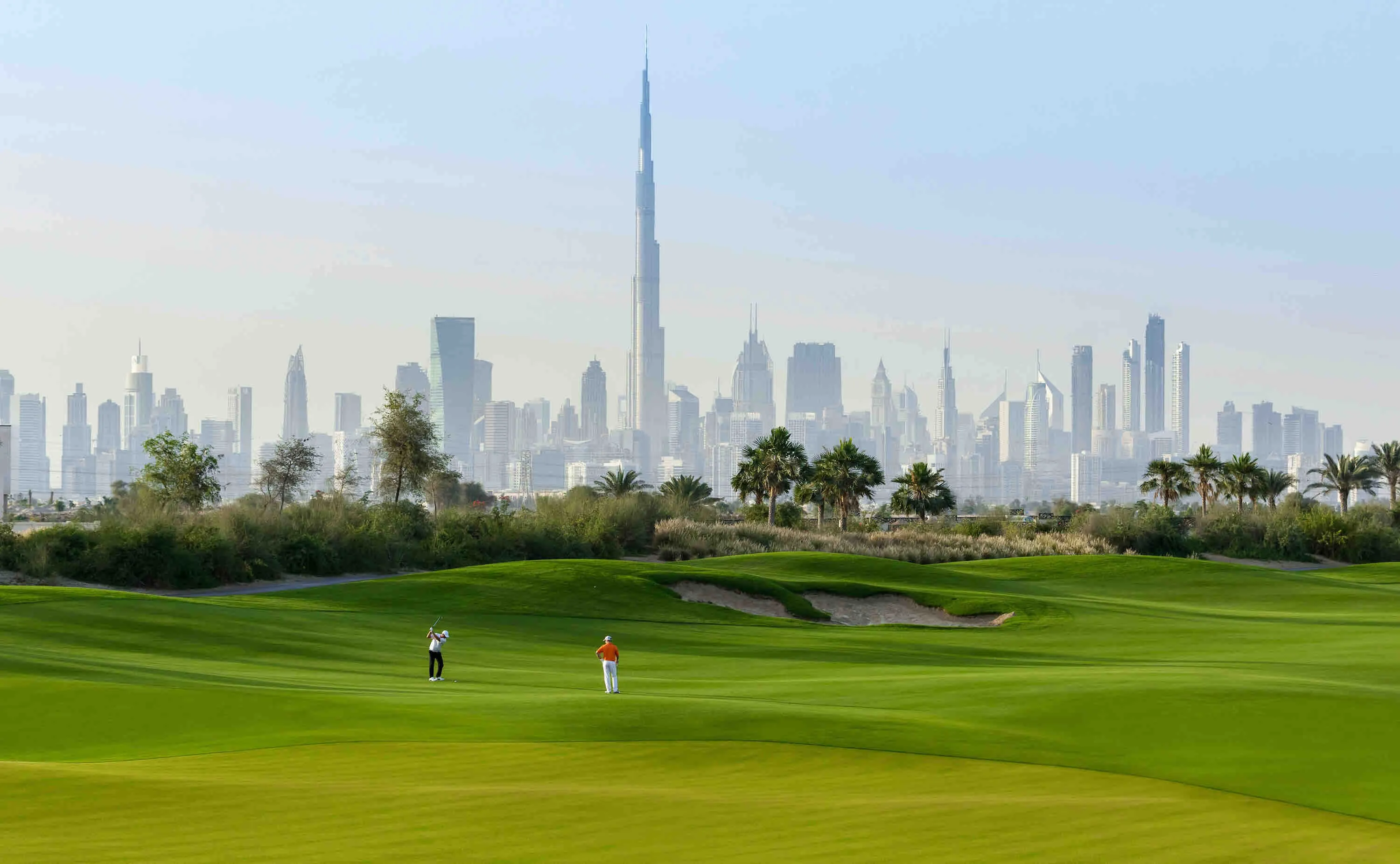 Golfers on the Dubai Hills course with the Burj Khalifa skyline behind